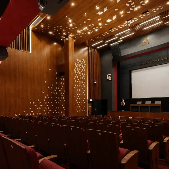 تصویر سه‌بعدی فوتورئال از سالن همایش با متریال چوب، کف‌پوش قرمز و چیدمان منظم صندلی‌ها؛ نمونه طراحی حرفه‌ای فضای فرهنگی و رویداد.